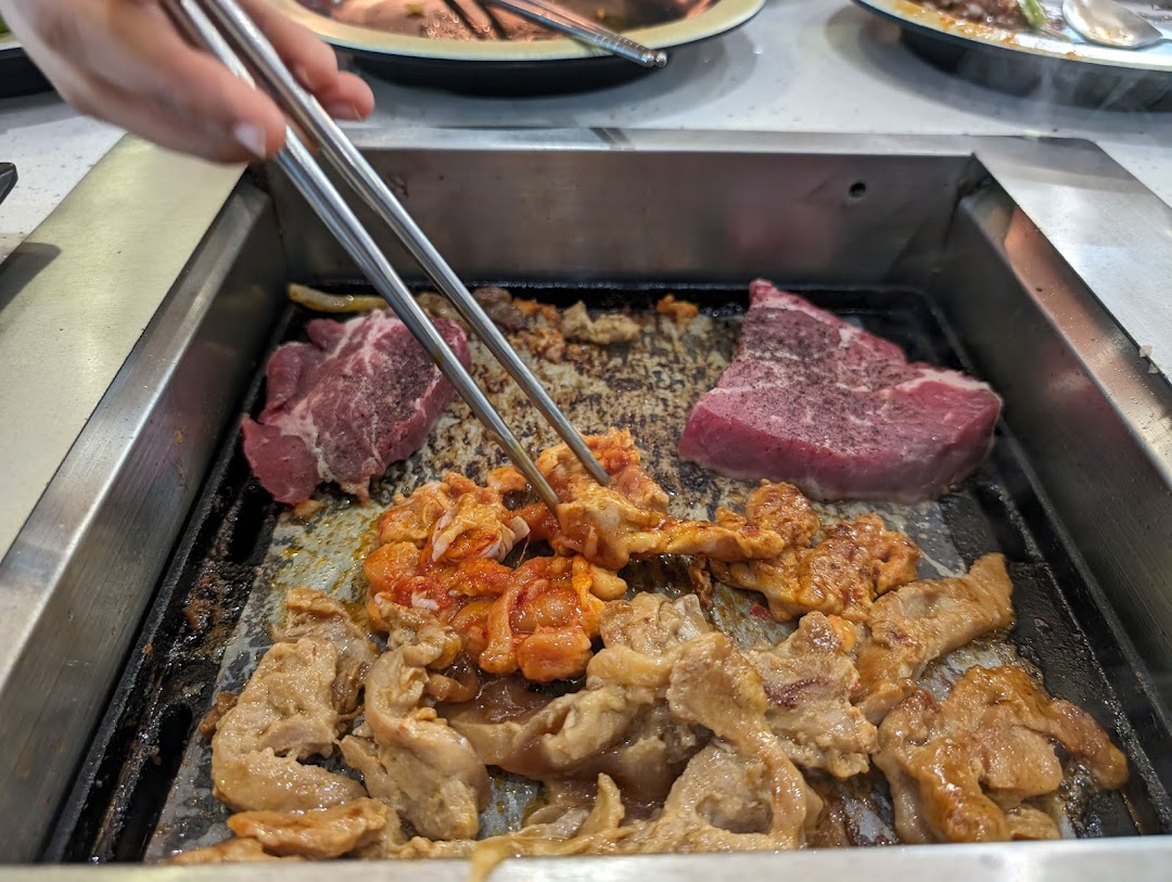 Various meats, including beef and marinated chicken, sizzling on a hot grill with chopsticks.