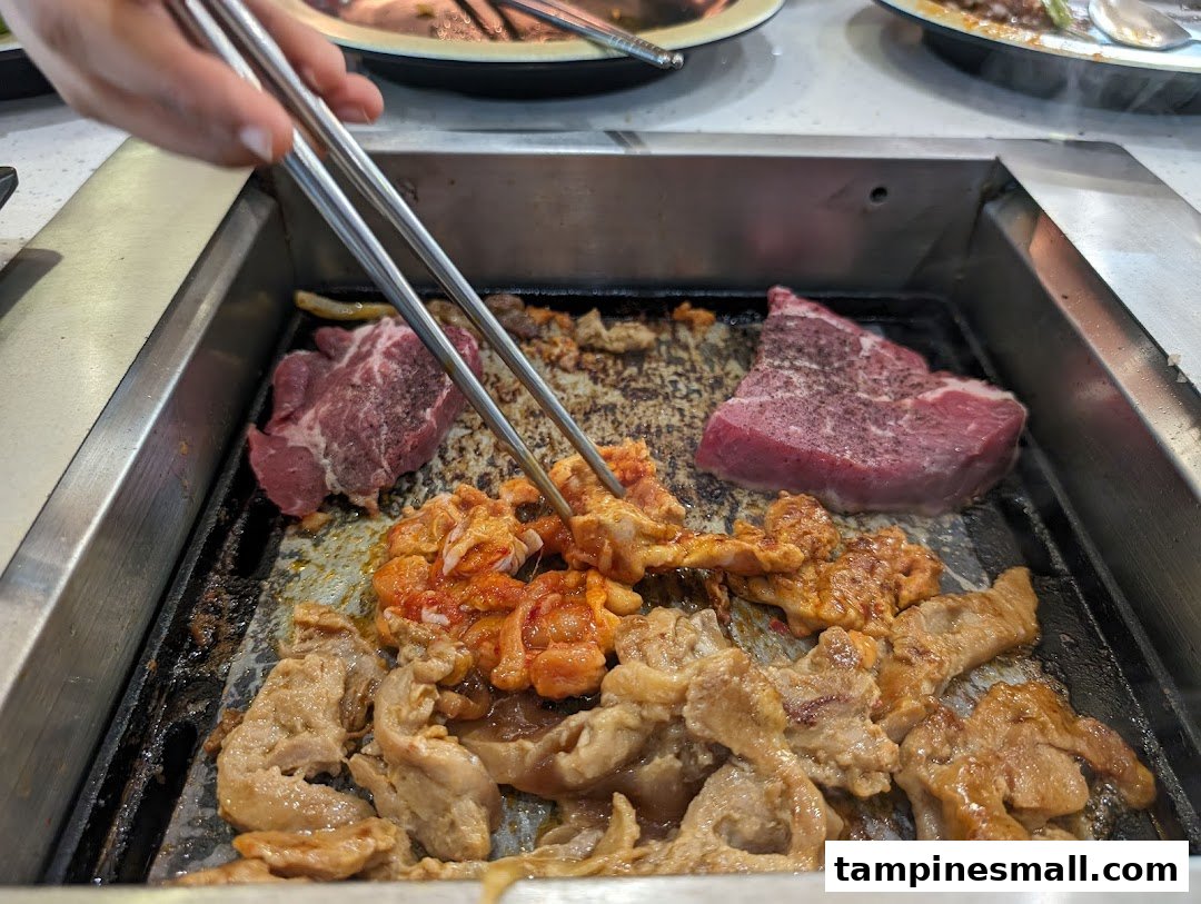 Various meats, including beef and marinated chicken, sizzling on a hot grill with chopsticks.