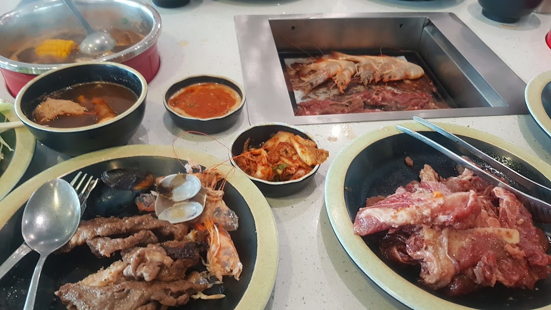 A table laden with hotpot, grill, raw meats, seafood, and side dishes for a buffet experience.