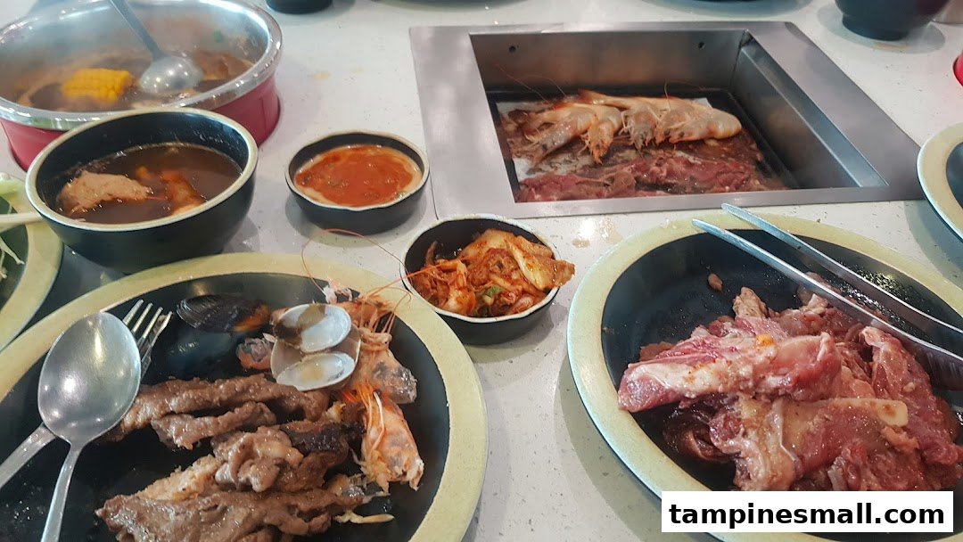 A table laden with hotpot, grill, raw meats, seafood, and side dishes for a buffet experience.