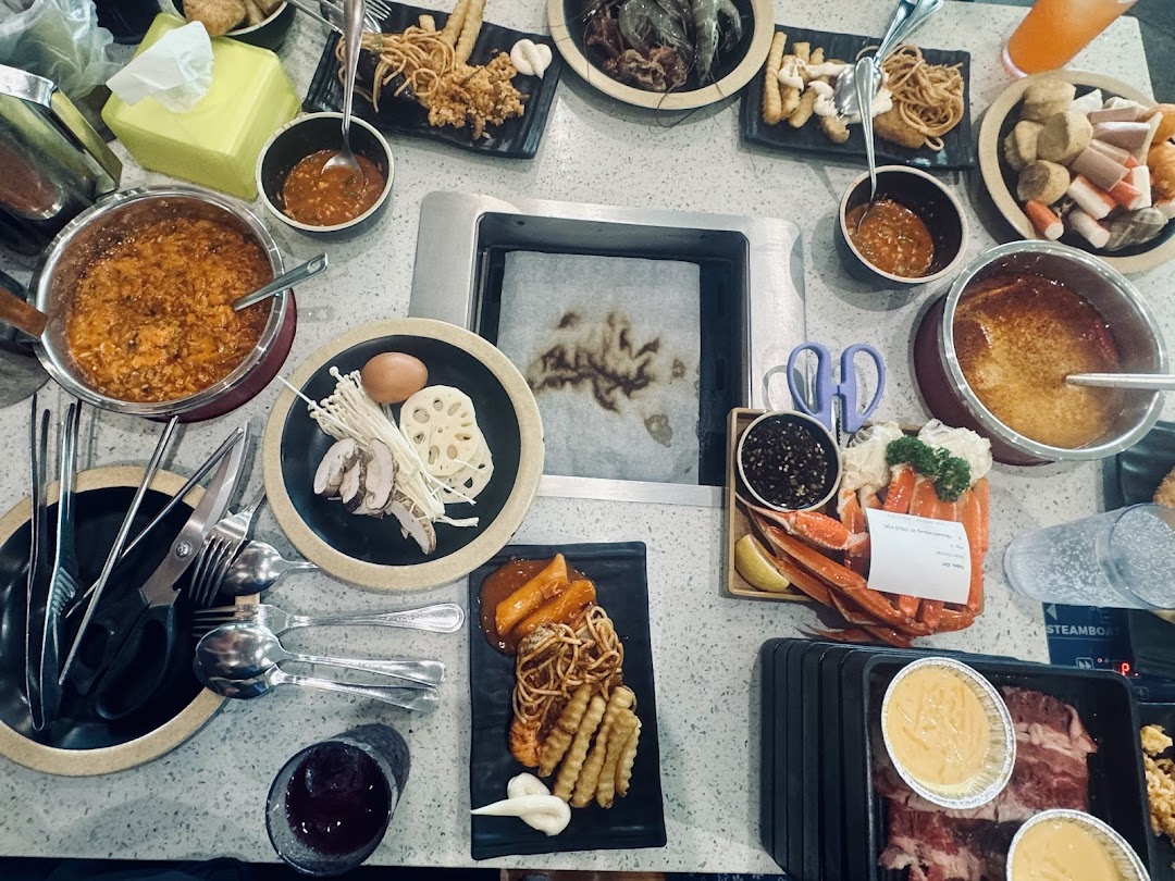 A table filled with a variety of hotpot and grill ingredients, cooked food, and sauces at Seoul Garden.