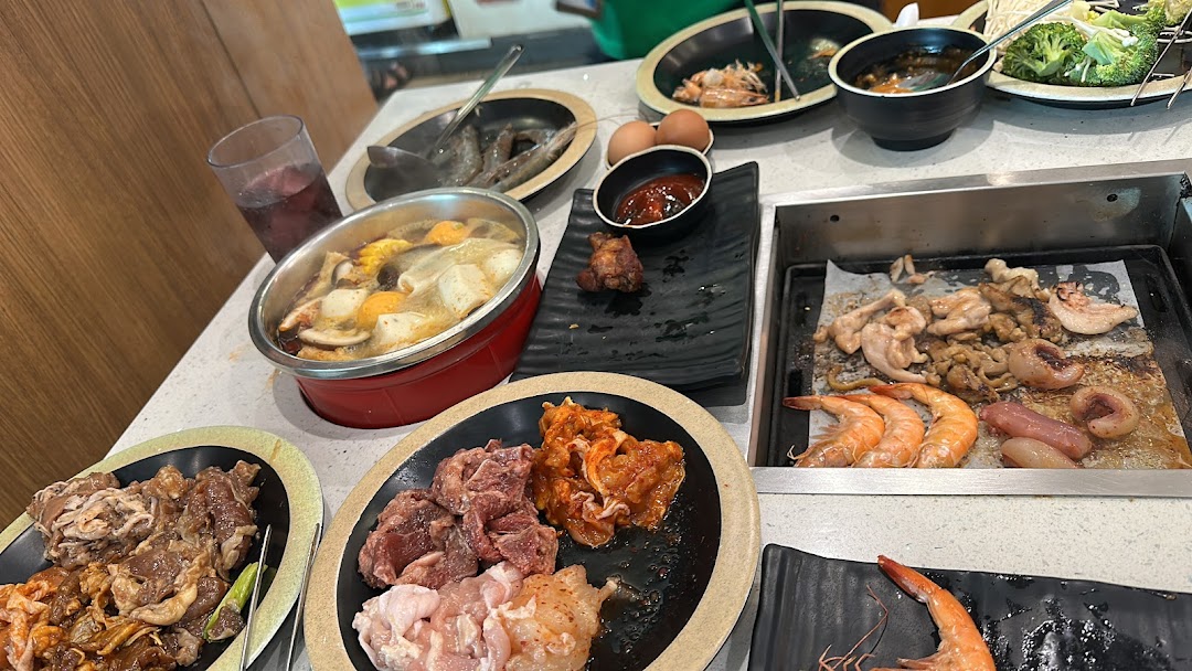 A table laden with raw meats, seafood, and vegetables for a hotpot and grill buffet experience.