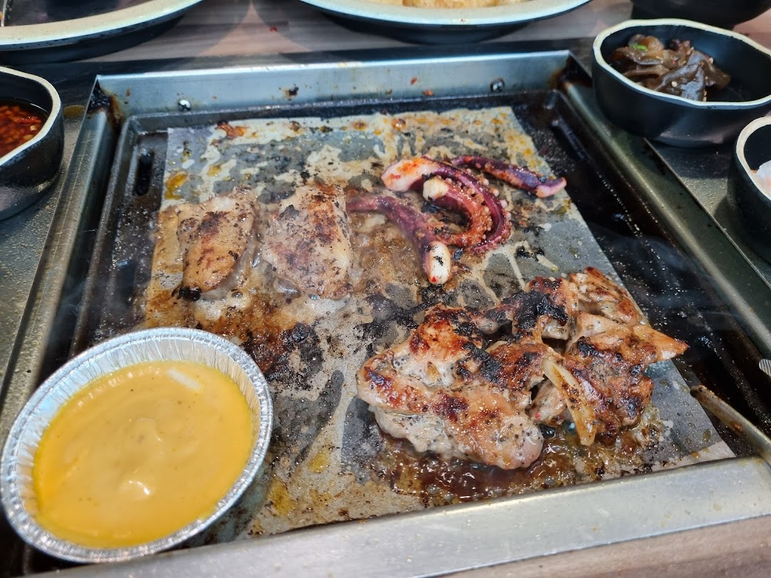 Grilled meats and seafood cooking on a hot plate with a dipping sauce at Seoul Garden.