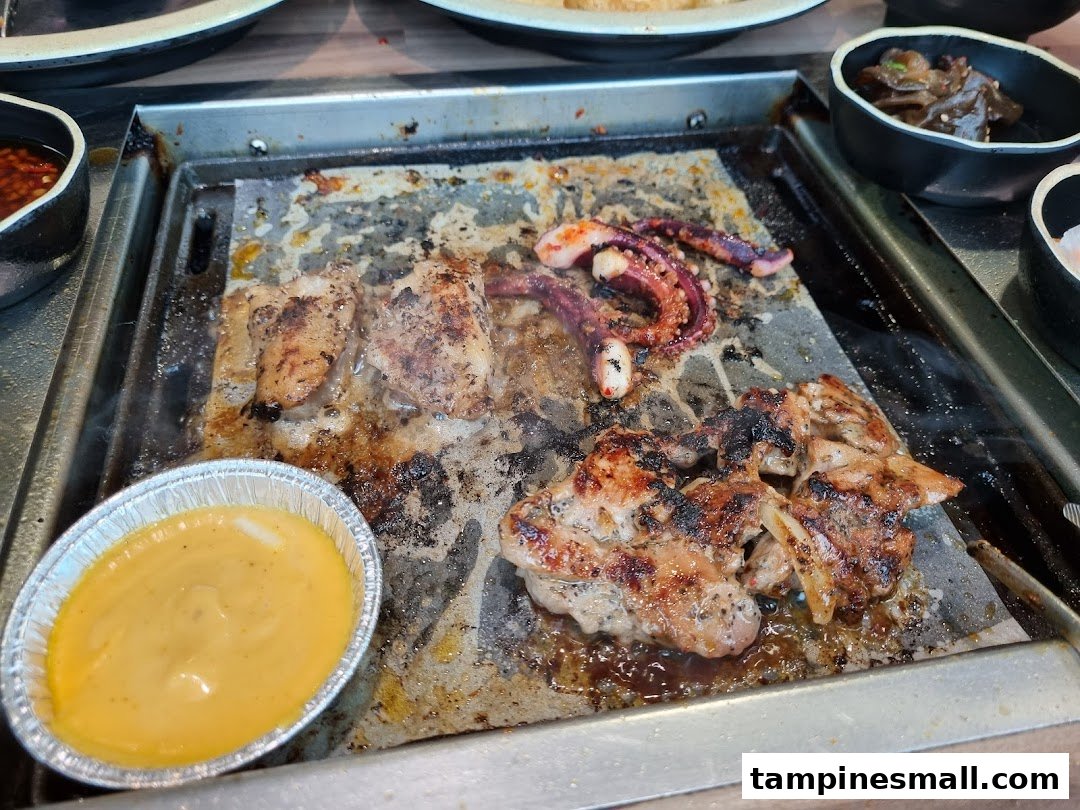Grilled meats and seafood cooking on a hot plate with a dipping sauce at Seoul Garden.