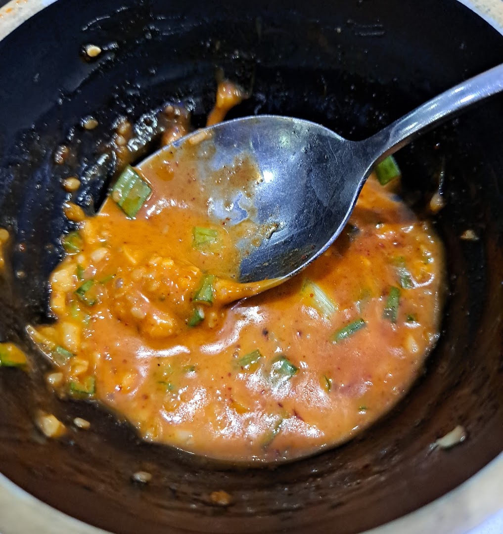 A close-up of a bowl containing a savory orange sauce with green herbs and a spoon.