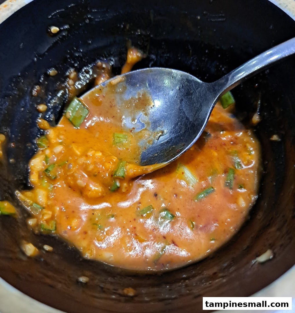 A close-up of a bowl containing a savory orange sauce with green herbs and a spoon.