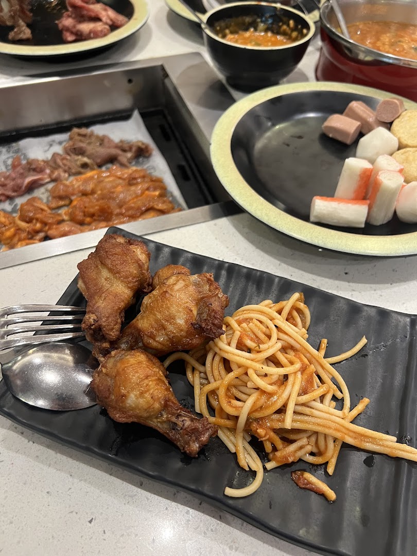 A close-up of fried chicken wings and spaghetti on a plate, with hotpot ingredients and raw meats in the background.