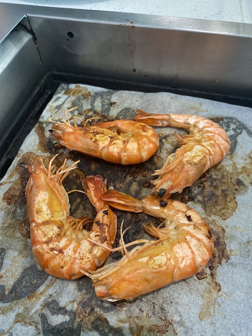 Four succulent grilled prawns cooking on a hot plate, showcasing their vibrant orange color and grill marks.