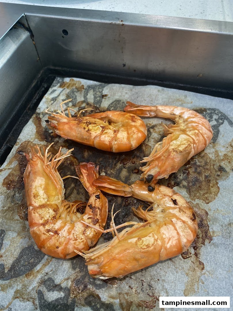 Four succulent grilled prawns cooking on a hot plate, showcasing their vibrant orange color and grill marks.