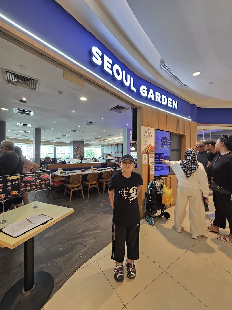 A young boy stands in front of the brightly lit Seoul Garden restaurant entrance at Tampines Mall.