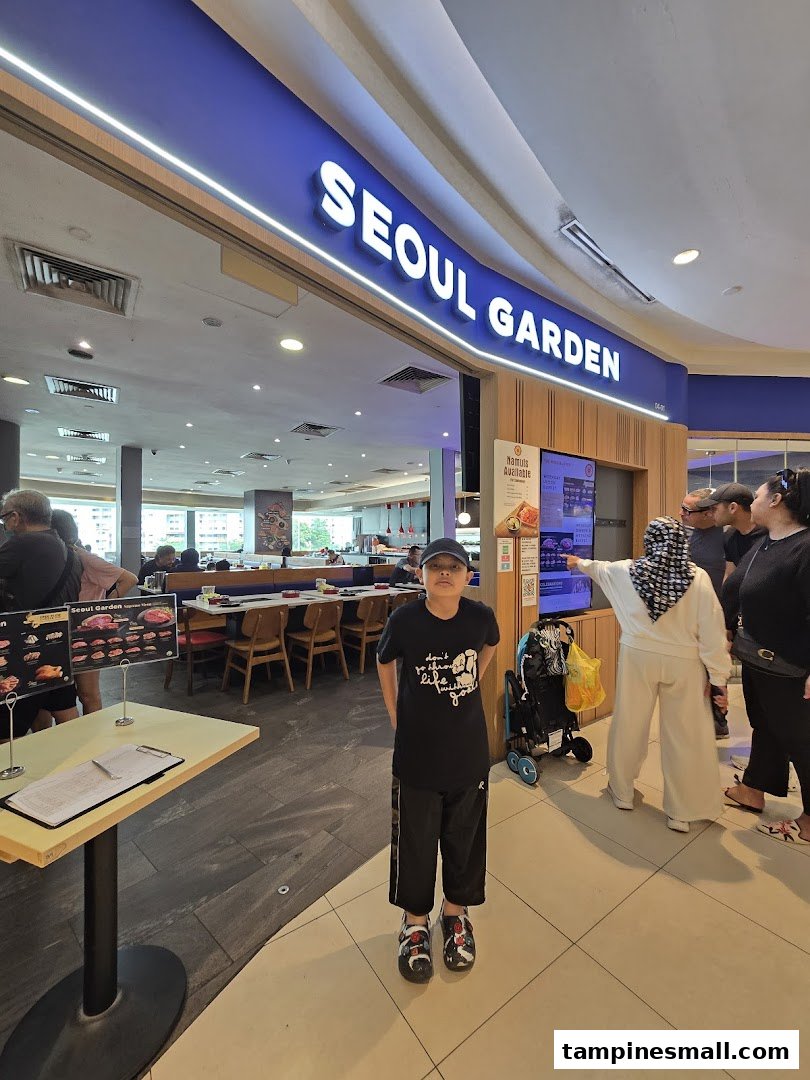 A young boy stands in front of the brightly lit Seoul Garden restaurant entrance at Tampines Mall.