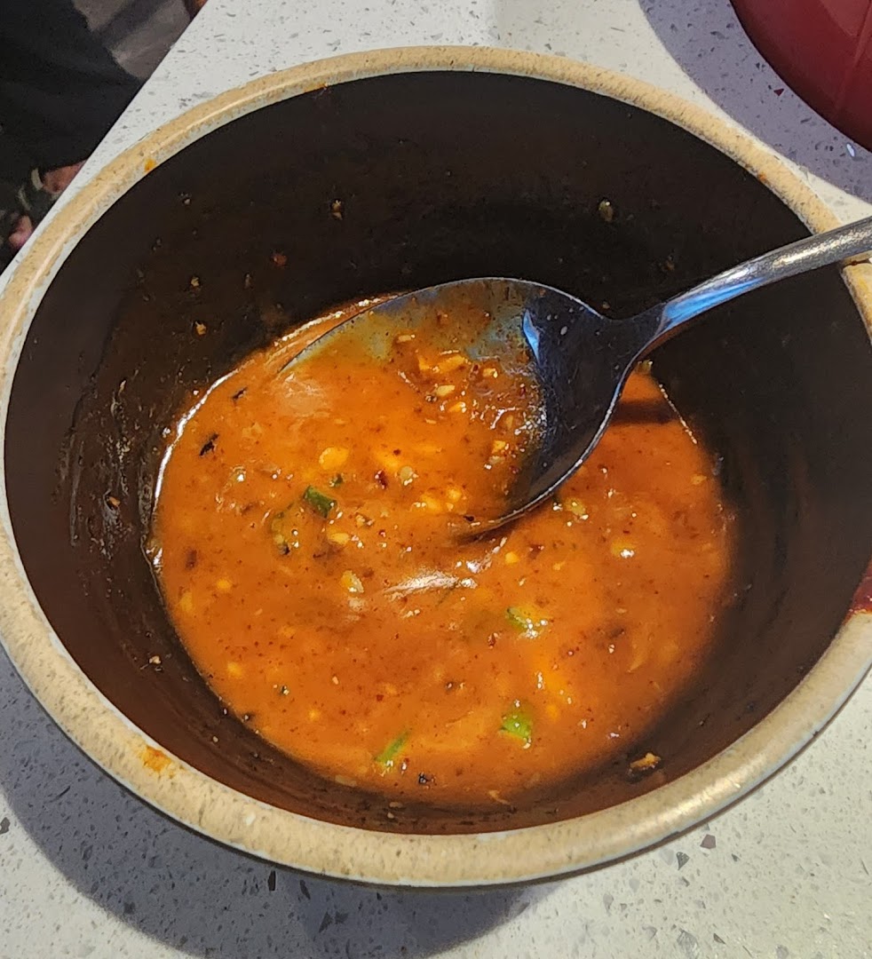 A close-up shot of a vibrant orange, spicy sauce or soup in a dark bowl with a spoon.