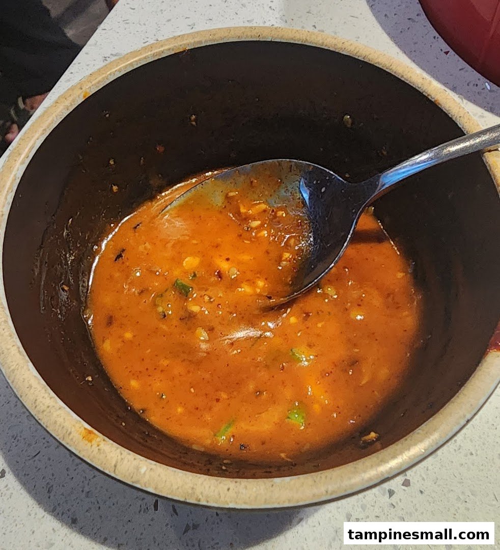 A close-up shot of a vibrant orange, spicy sauce or soup in a dark bowl with a spoon.