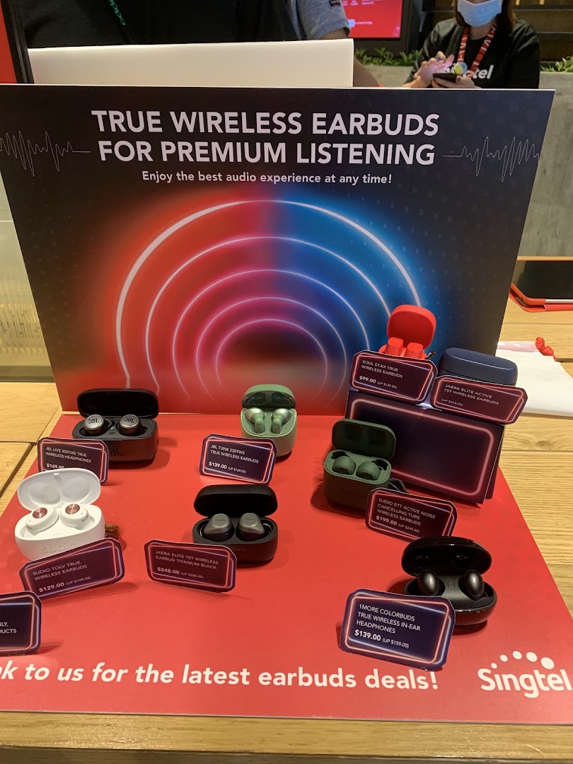 A display of various true wireless earbuds with prices and a promotional sign at Singtel.
