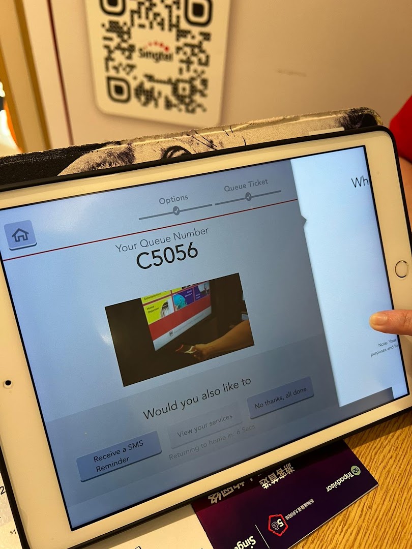 An iPad displaying a Singtel queue number (C5056) and service options for customers.