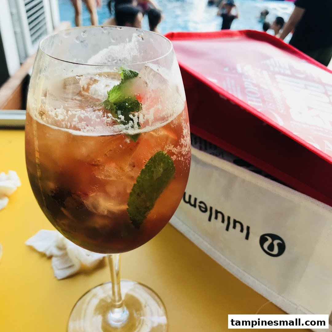 A refreshing drink with mint and ice, a Lululemon bag, and a pool in the background.