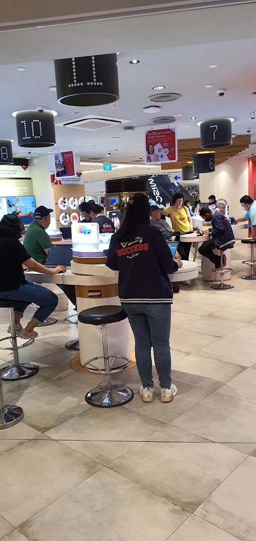 Customers and staff interact at service counters within the Singtel Shop, showcasing a busy retail environment.