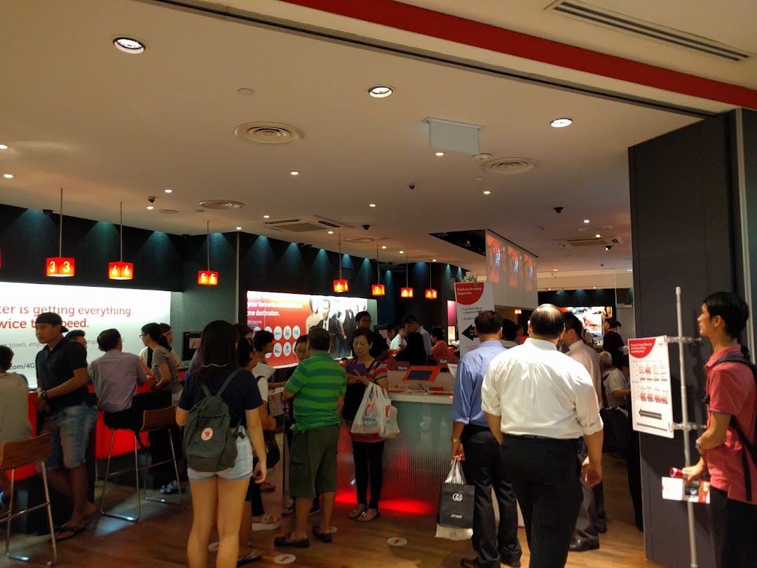 Interior view of a busy Singtel Shop with customers and staff, showcasing service counters and digital displays.