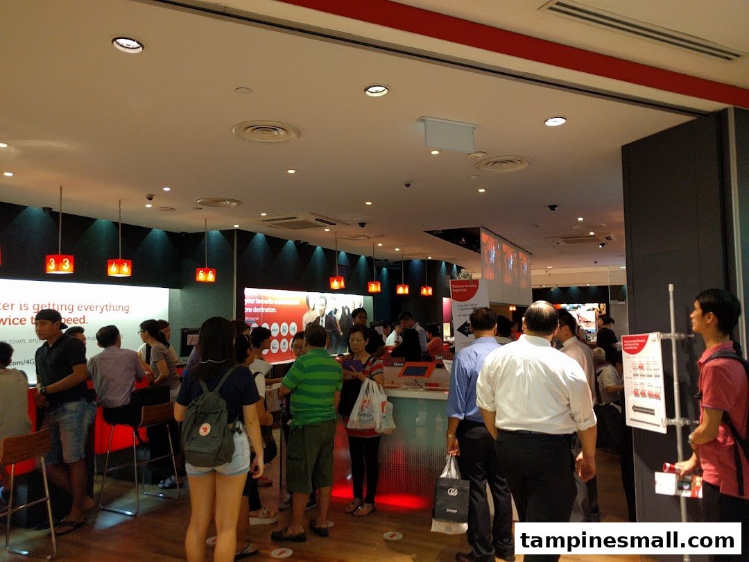 Interior view of a busy Singtel Shop with customers and staff, showcasing service counters and digital displays.