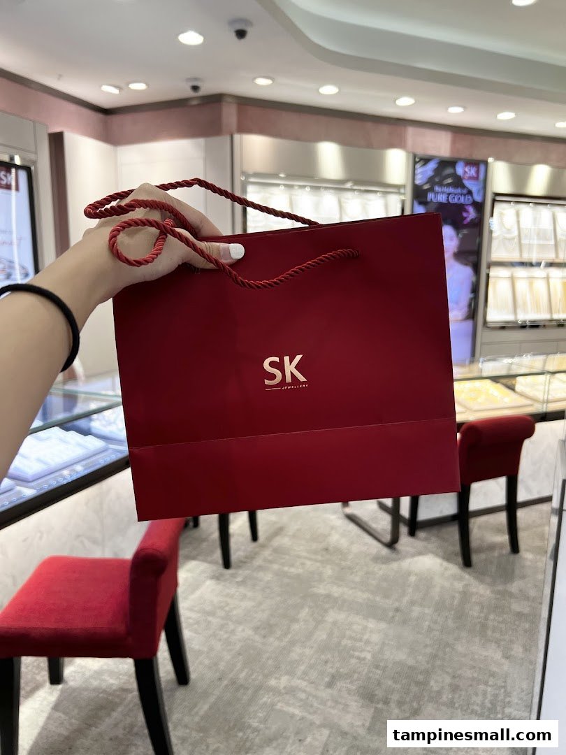 A person holds a red SK Jewellery shopping bag inside the store, showcasing the brand's packaging.