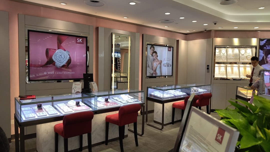 Interior view of SK Gold jewelry store with display cases, digital screens, and a staff member.
