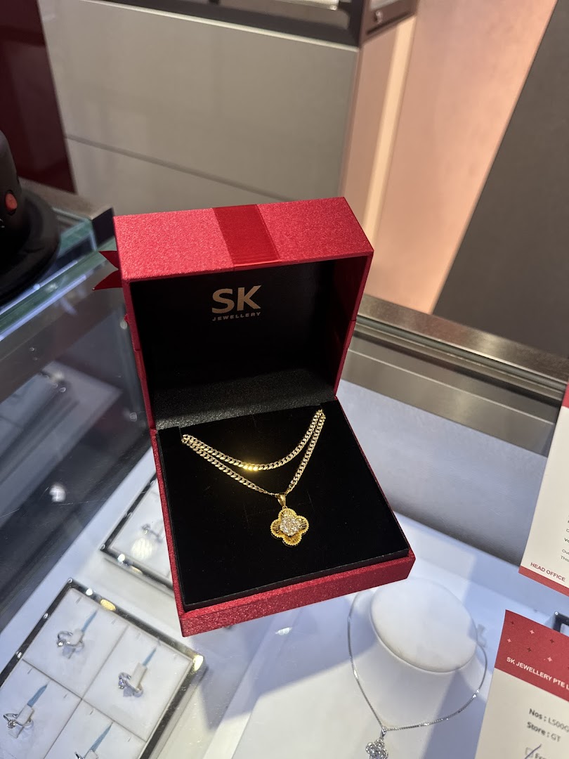 A beautiful gold necklace with a clover pendant displayed in a red SK Jewellery gift box.
