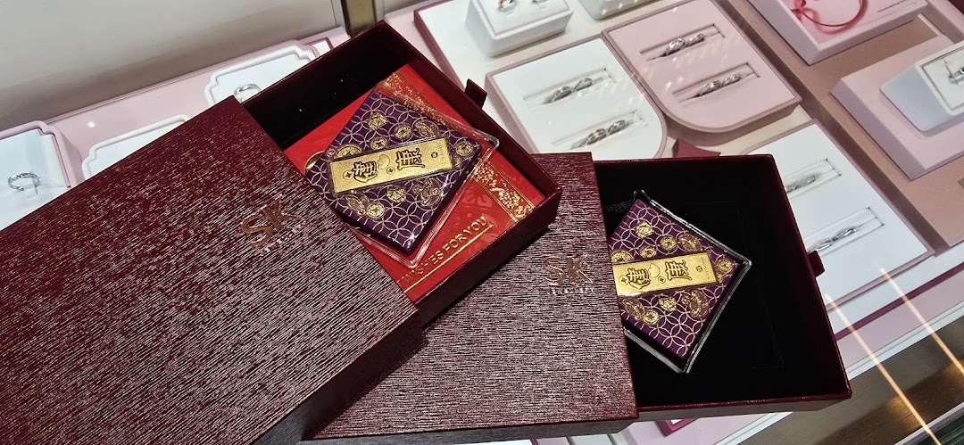 A gold bar in a decorative box with other jewelry displays in the background at SK Jewellery.