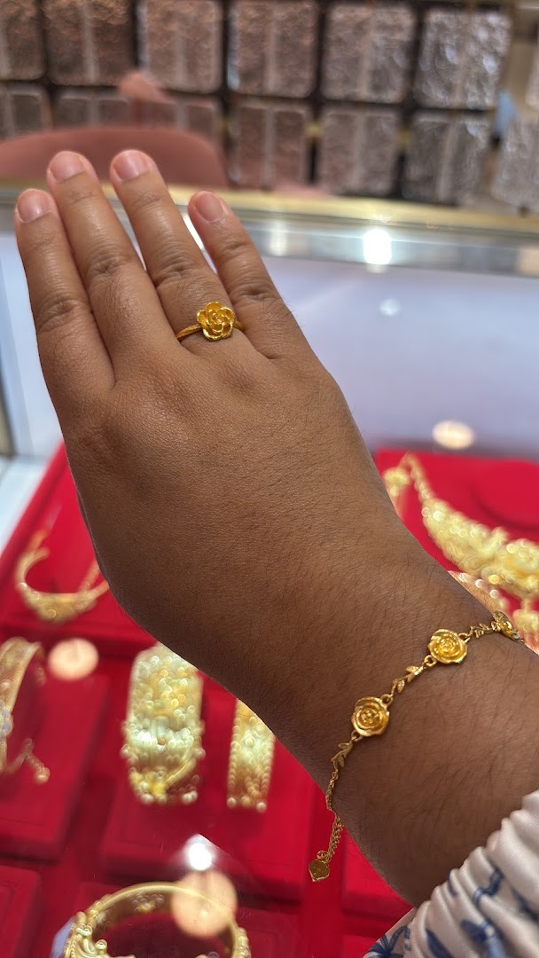 A hand adorned with a gold rose ring and matching bracelet, showcasing intricate jewelry designs.