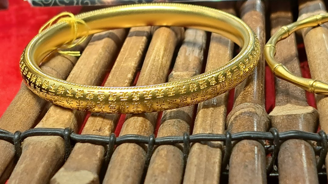 A close-up of an intricately engraved gold bracelet displayed on a bamboo-style stand.