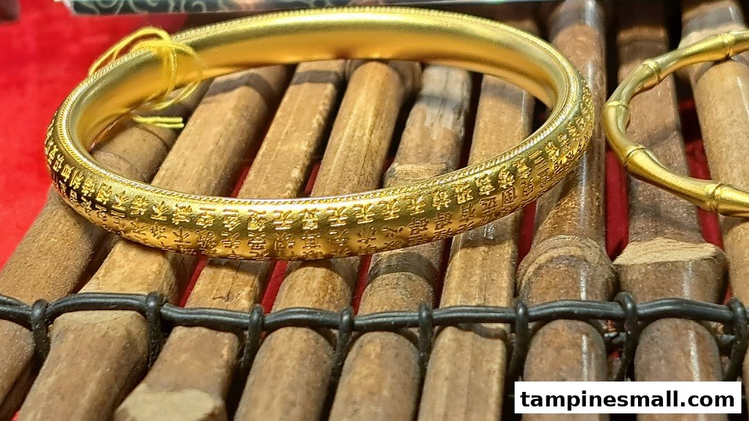 A close-up of an intricately engraved gold bracelet displayed on a bamboo-style stand.