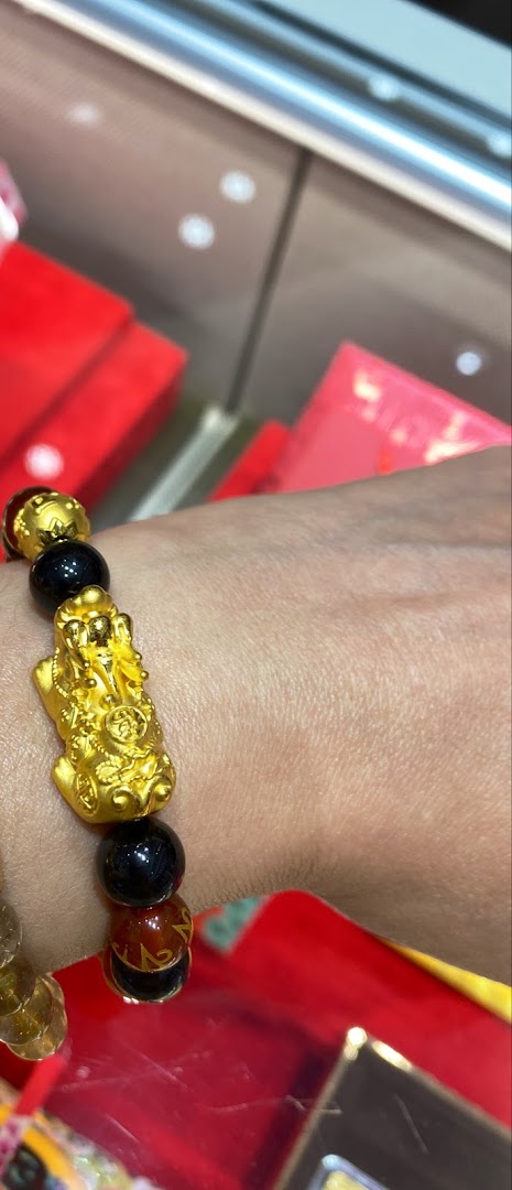 A person's wrist adorned with a gold Pixiu charm bracelet featuring black and brown beads.