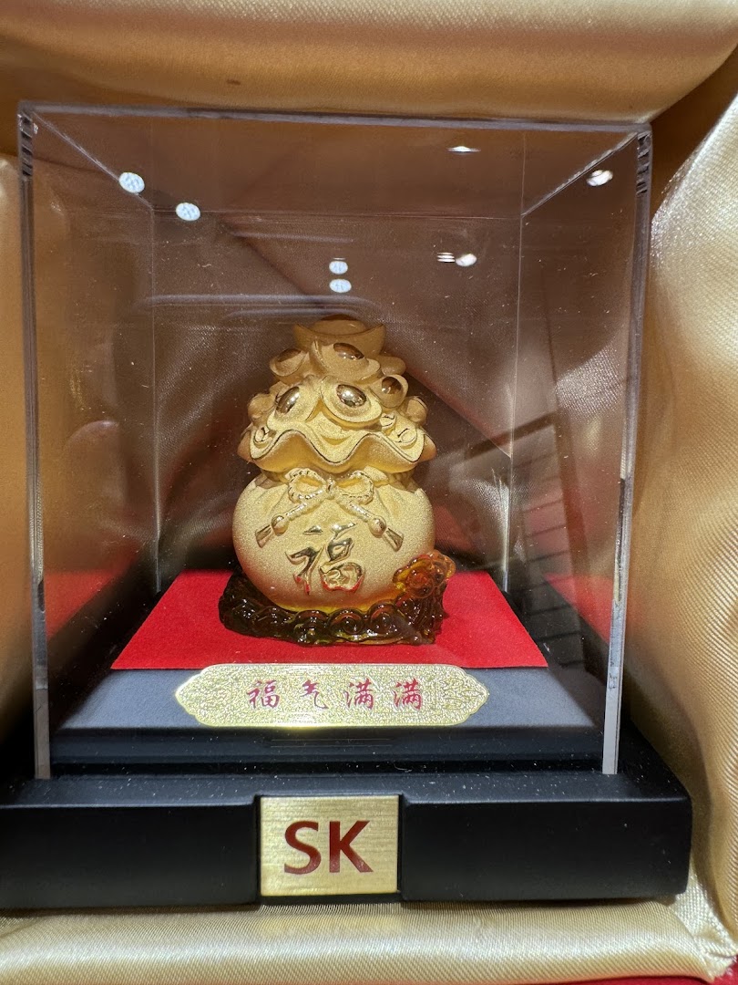 A golden prosperity bag figurine with Chinese characters displayed in a clear case.