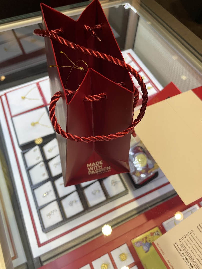 A red shopping bag rests on a display case showcasing various gold and diamond jewelry pieces.