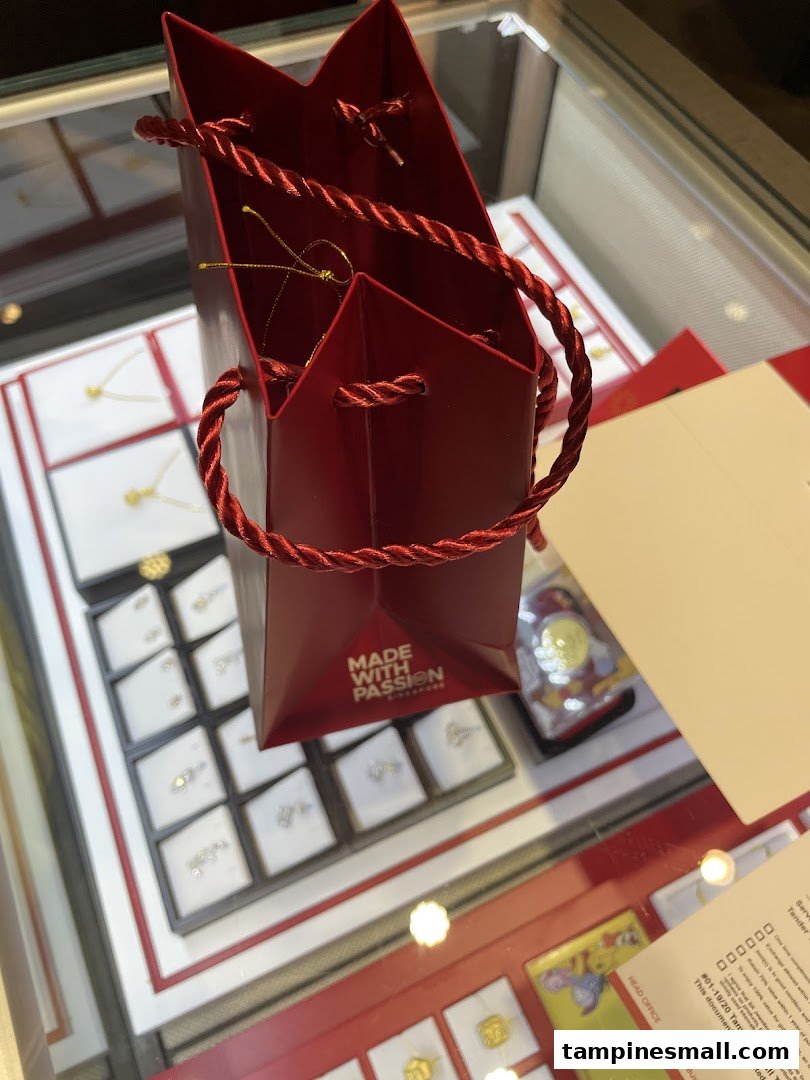 A red shopping bag rests on a display case showcasing various gold and diamond jewelry pieces.