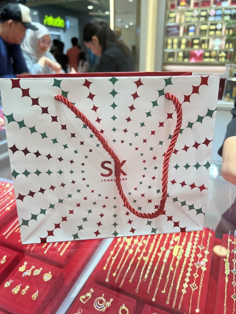 An SK Jewellery shopping bag sits on a display case showcasing various gold jewelry pieces.