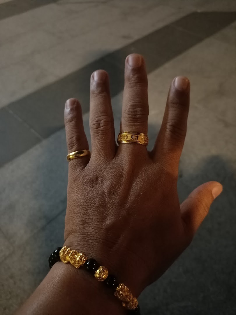 A hand adorned with two gold rings and a black and gold beaded bracelet.