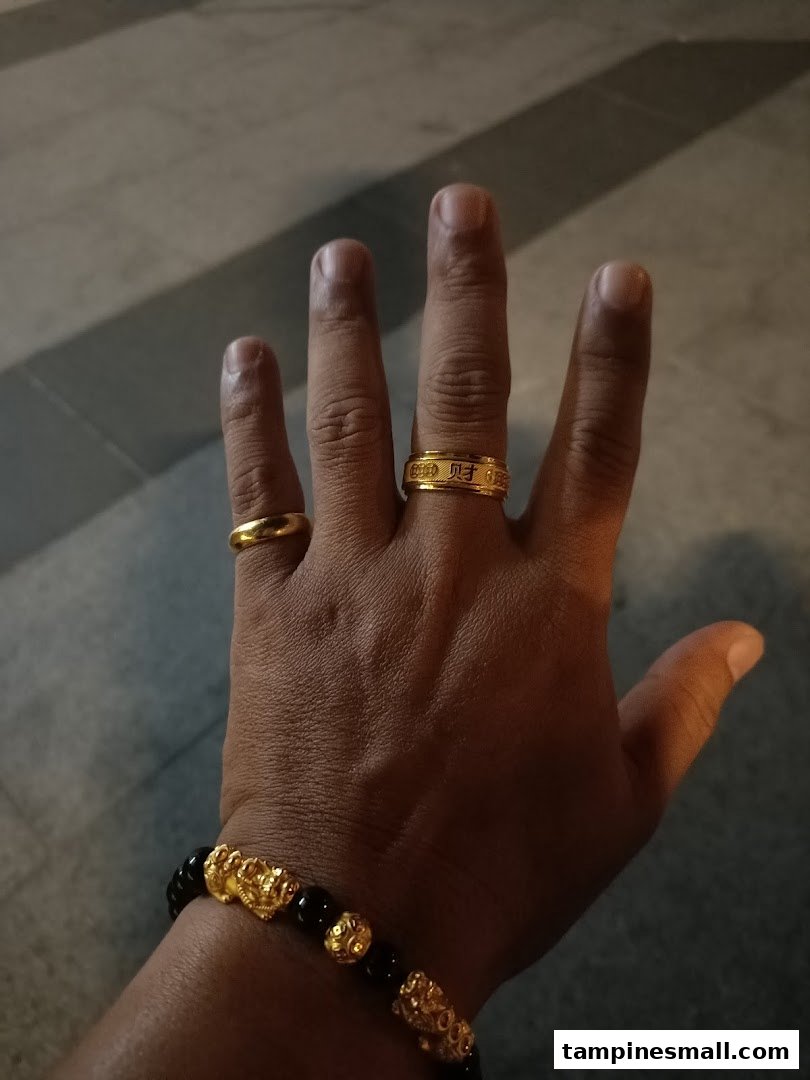 A hand adorned with two gold rings and a black and gold beaded bracelet.