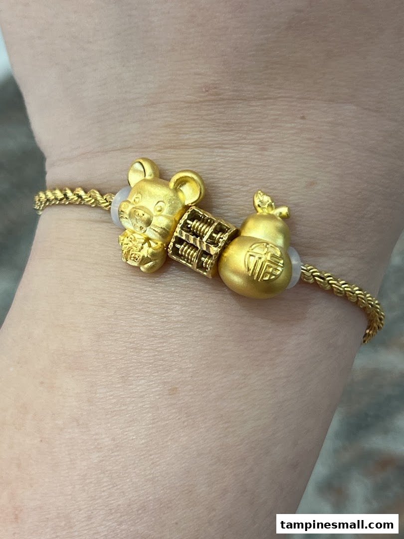 Close-up of a gold bracelet featuring a mouse, abacus, and gourd charm on a wrist.