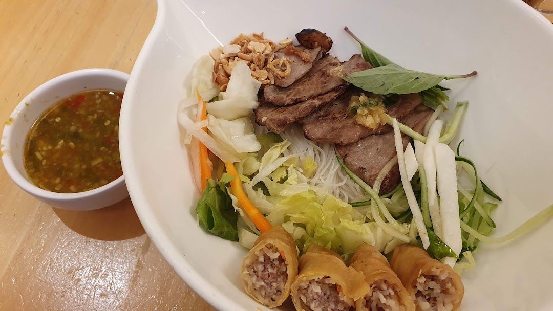 A vibrant bowl of Vietnamese vermicelli noodles with grilled meat, fresh vegetables, crispy spring rolls, and a side of dipping sauce.