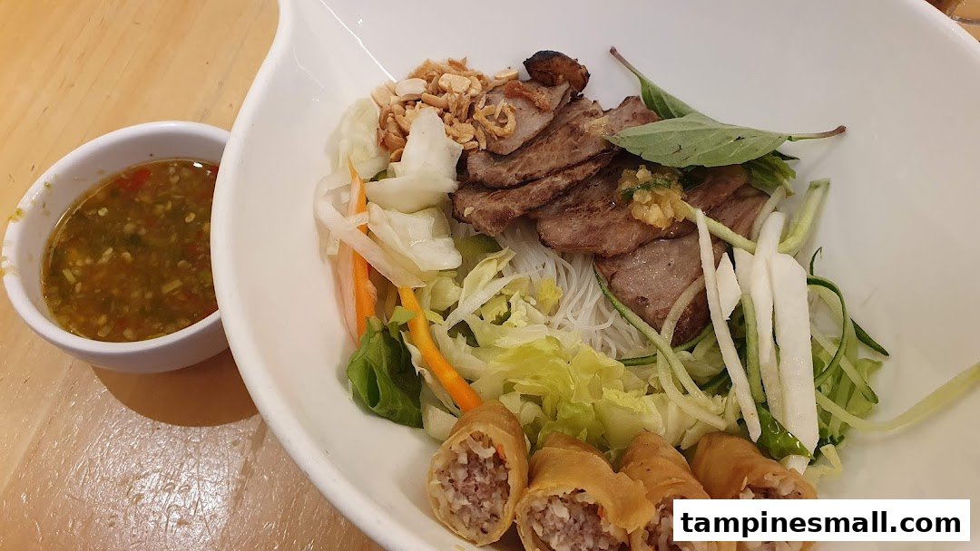 A vibrant bowl of Vietnamese vermicelli noodles with grilled meat, fresh vegetables, crispy spring rolls, and a side of dipping sauce.