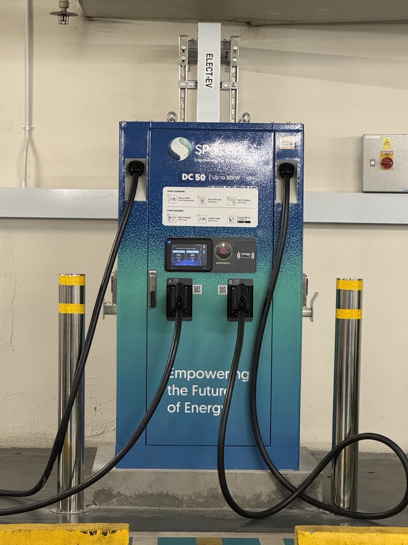 A modern SP Mobility DC 50 electric vehicle charging station with two charging cables in a parking area.