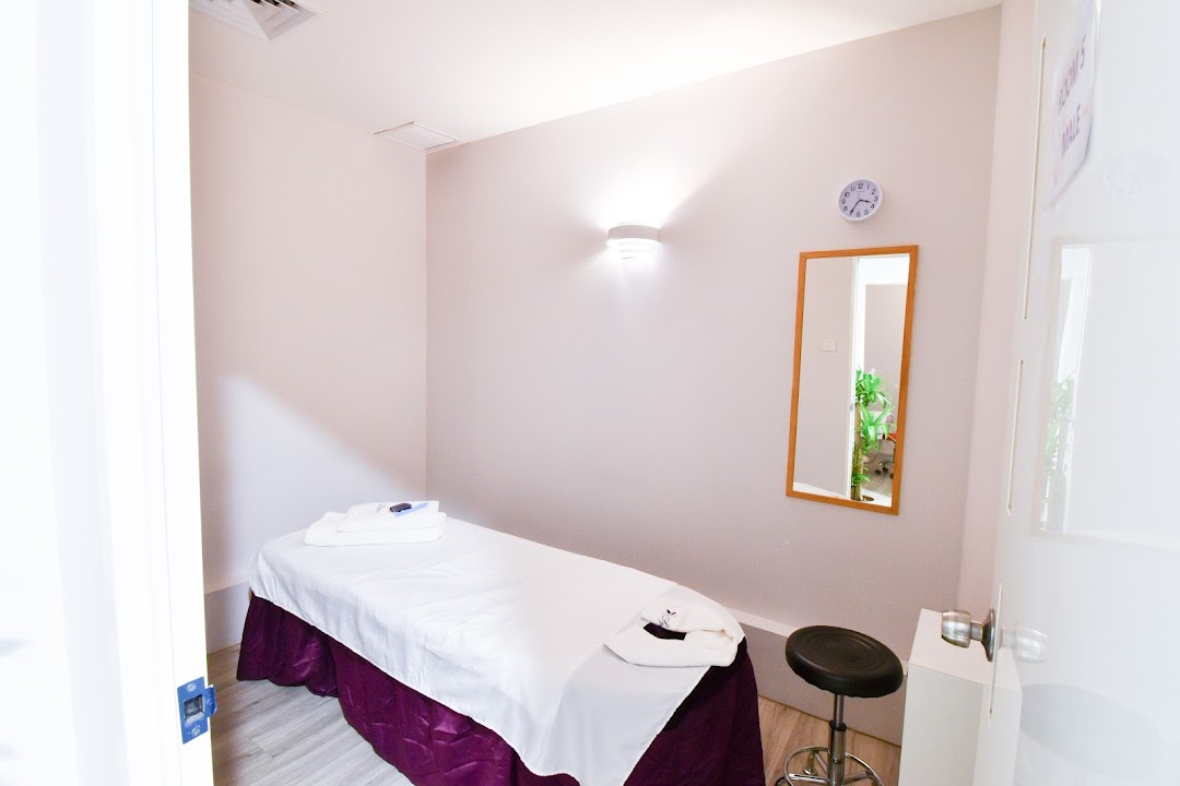A clean, well-lit treatment room with a massage bed, mirror, and stool.