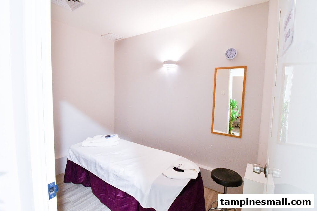 A clean, well-lit treatment room with a massage bed, mirror, and stool.