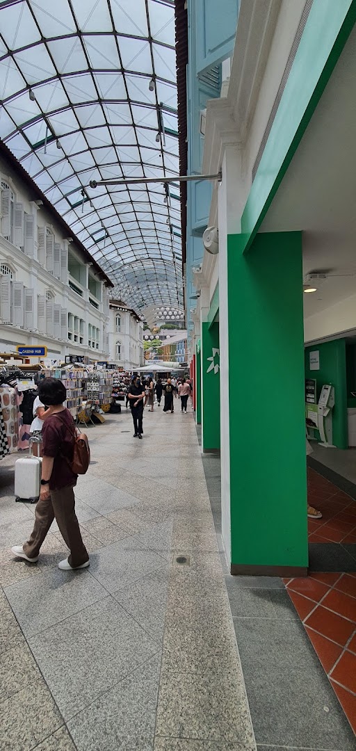 A bustling covered walkway in a mall, featuring a green pillar and self-service kiosks associated with StarHub.