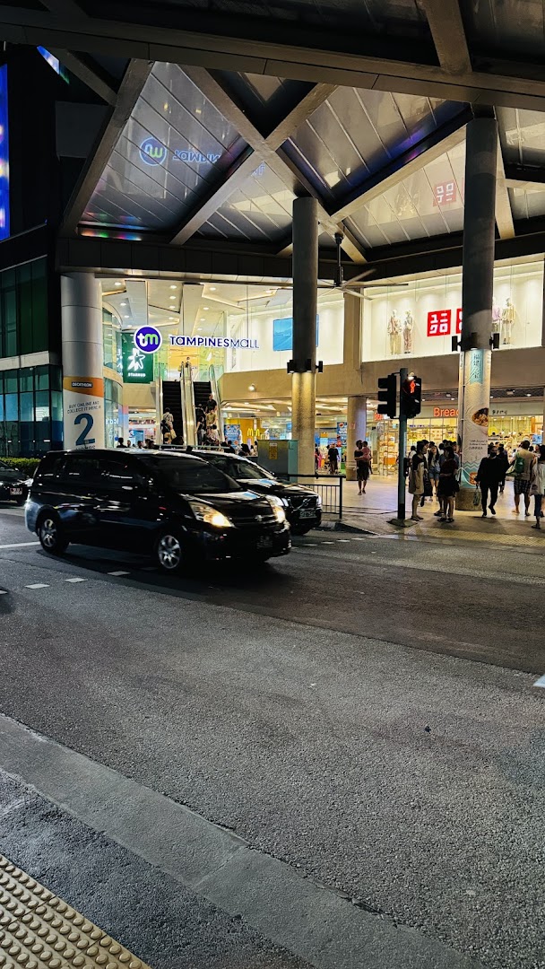 Evening view of Tampines Mall entrance, featuring StarHub and Uniqlo signs, with cars and pedestrians.