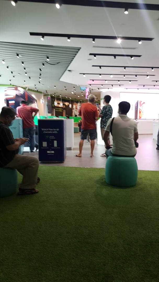 Interior view of StarHub store with customers browsing and waiting, featuring green carpet and seating.