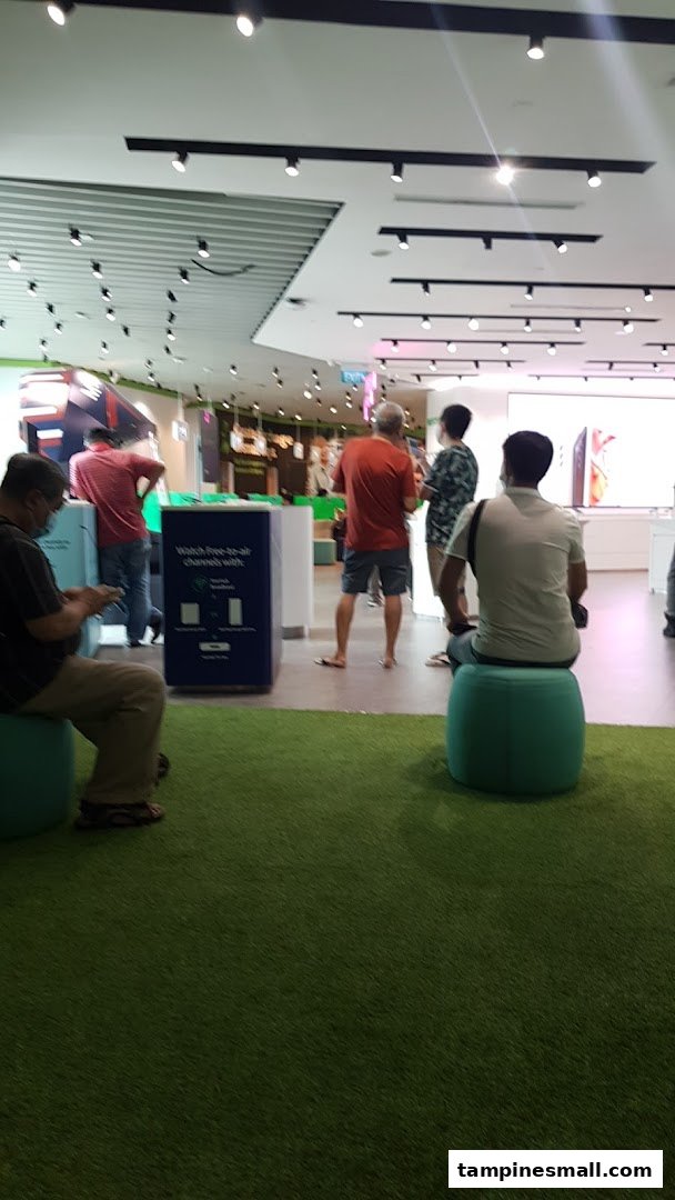 Interior view of StarHub store with customers browsing and waiting, featuring green carpet and seating.