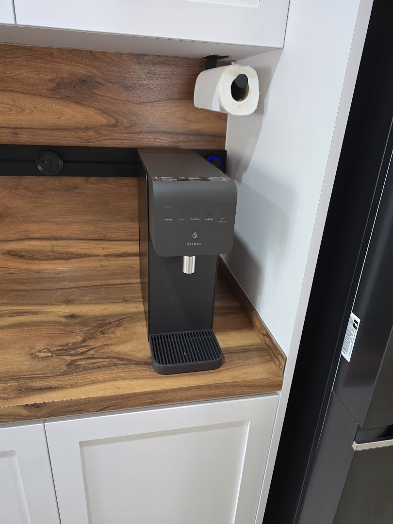 A black Sterra water dispenser on a wooden countertop in a modern kitchen display.