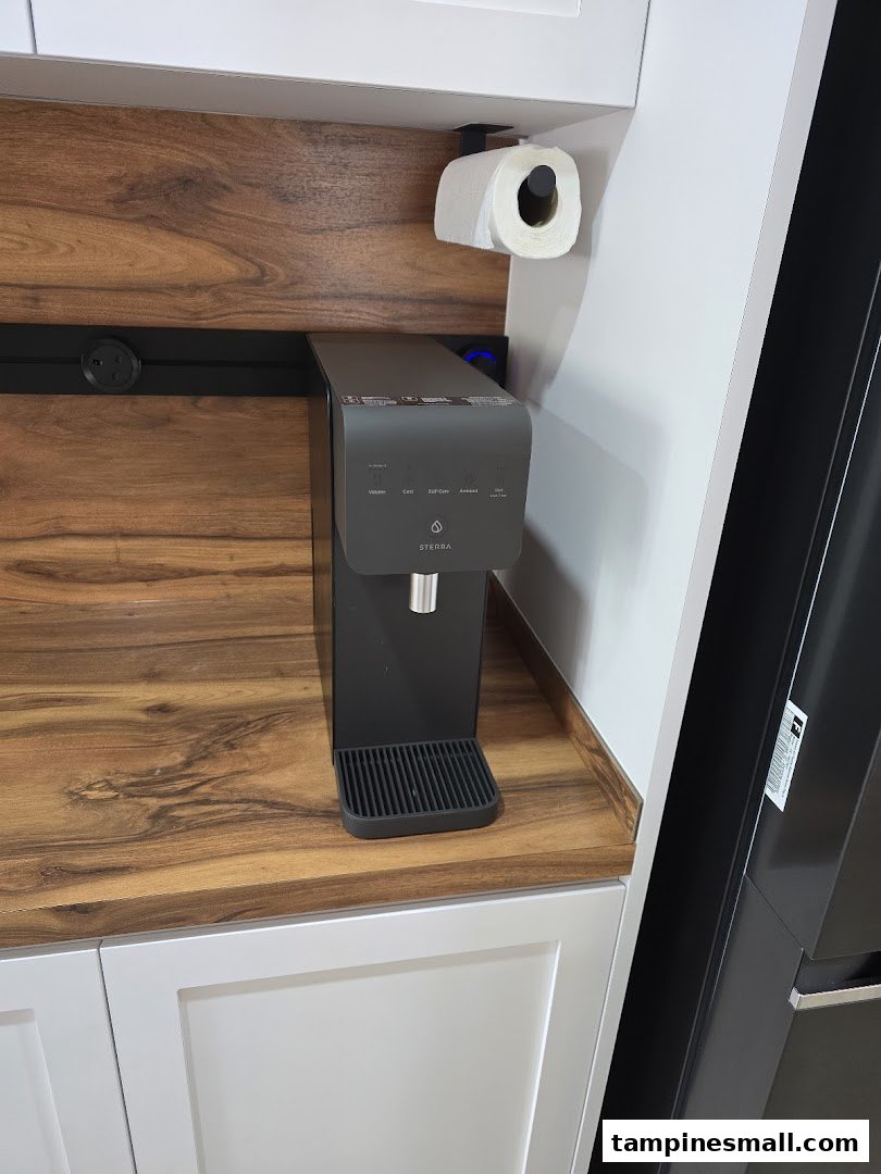 A black Sterra water dispenser on a wooden countertop in a modern kitchen display.