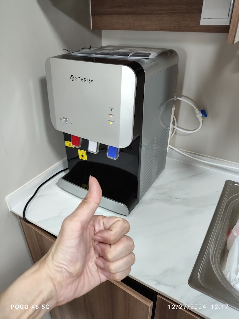 A Sterra water dispenser on a counter with a hand giving a thumbs-up.